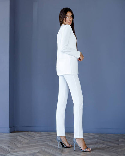 Woman wearing a white suit standing against a blue wall.