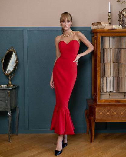 Woman in a red dress standing in an elegant room with wooden furniture and a mirror.