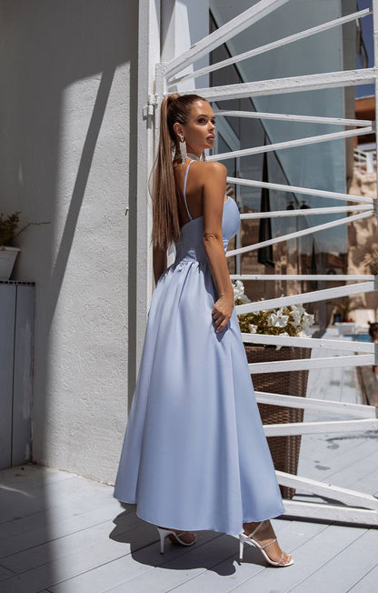 Woman in a light blue dress standing on a balcony with a white railing.