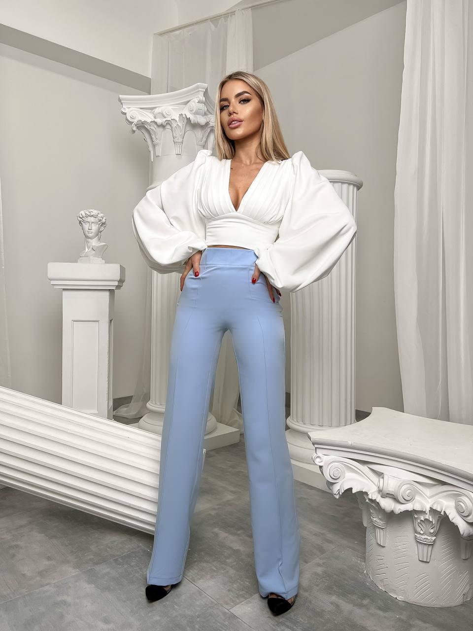 Woman wearing a white blouse and light blue pants in an elegant interior setting.