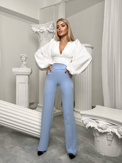 Woman wearing a white blouse and light blue pants in an elegant interior setting.