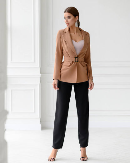 Woman wearing a tan blazer and black pants in a minimalistic setting