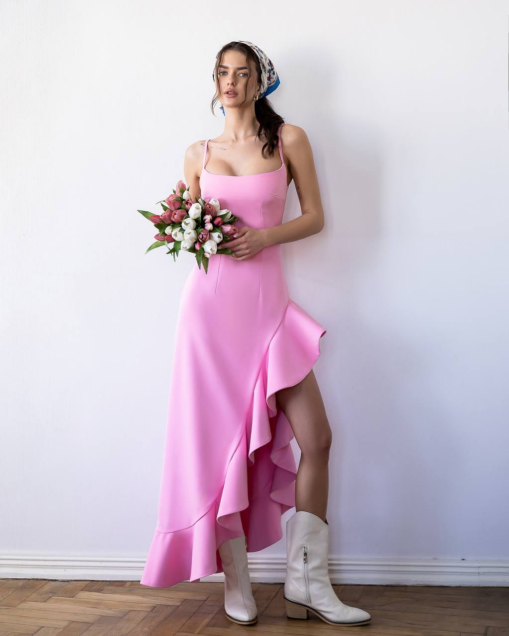 Woman in a pink dress holding flowers against a white wall