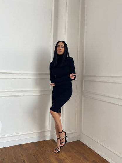 Woman in a black dress standing against a white paneled wall.