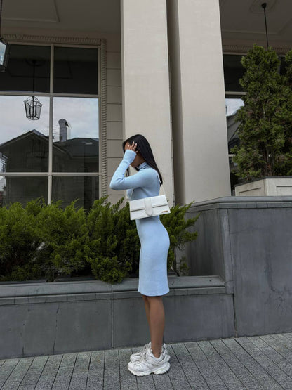 Woman in a light blue dress standing outside a building with greenery.