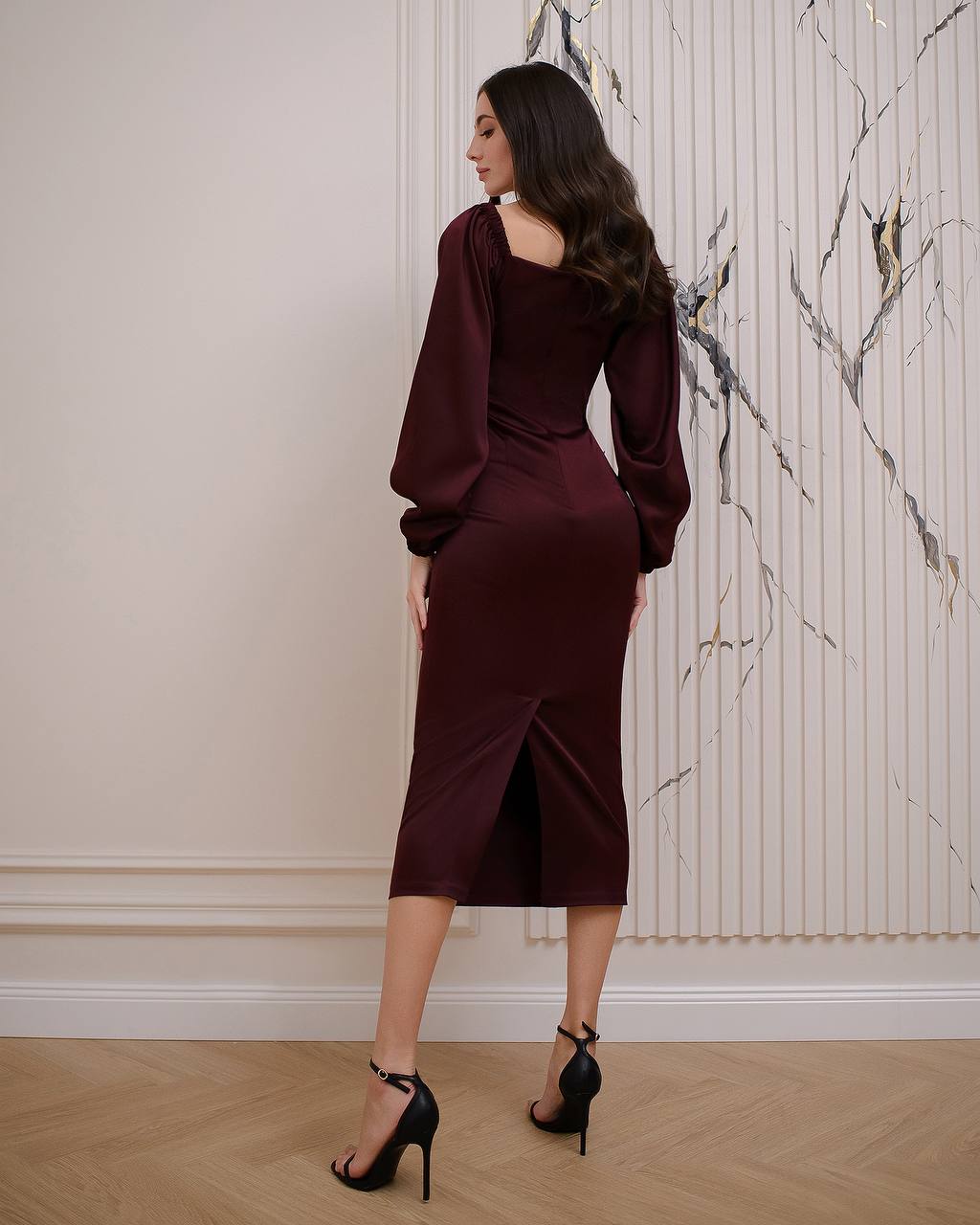 Woman wearing a burgundy dress standing in a room with marble-patterned wallpaper.