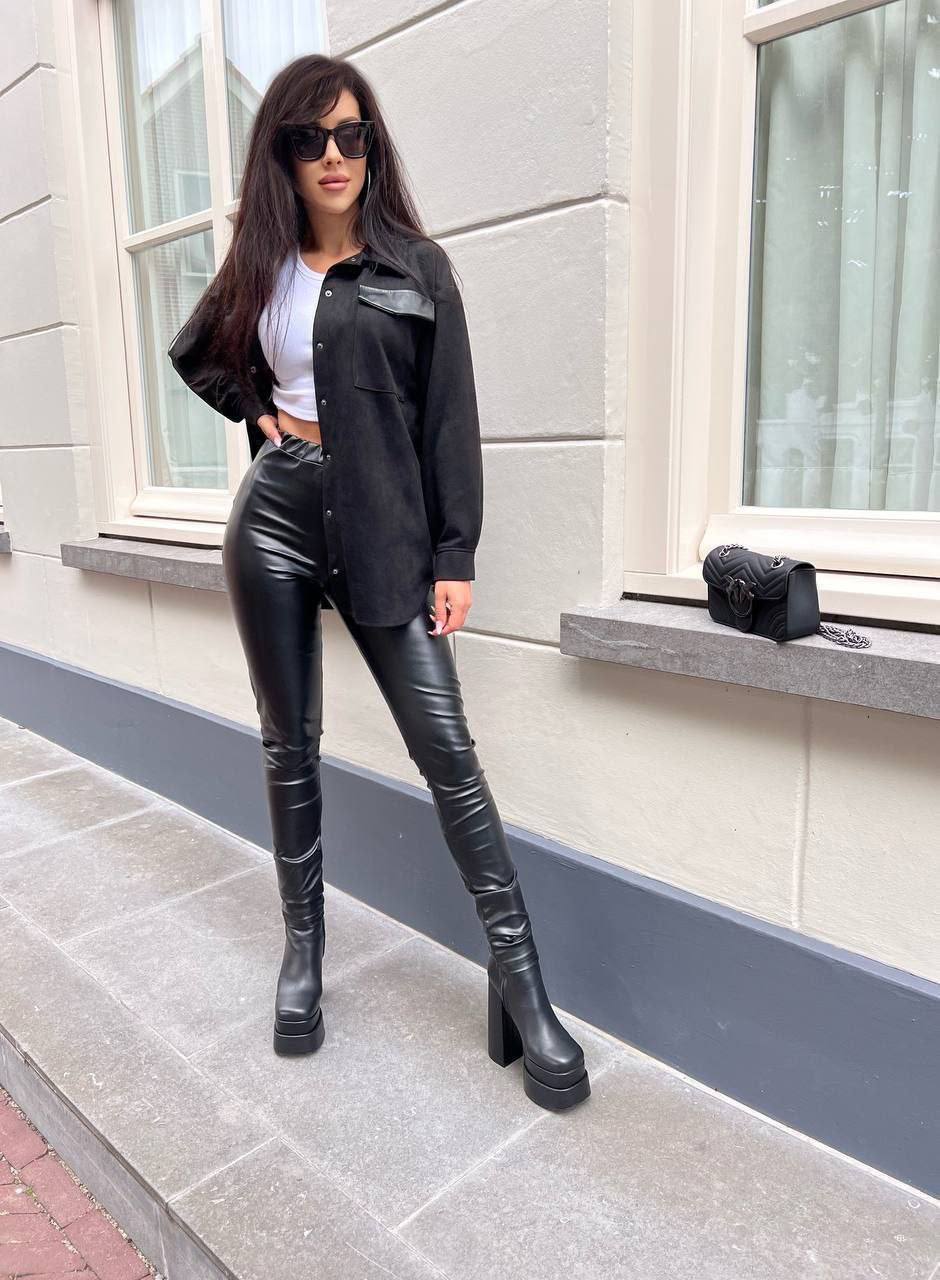 Woman in black leather outfit standing on a sidewalk with a building in the background