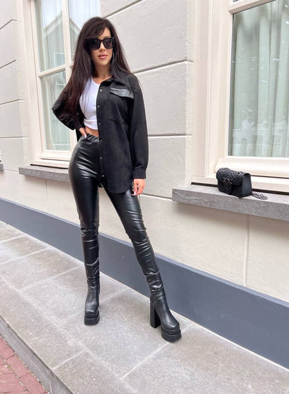 Woman in black leather outfit standing on a sidewalk with a building in the background
