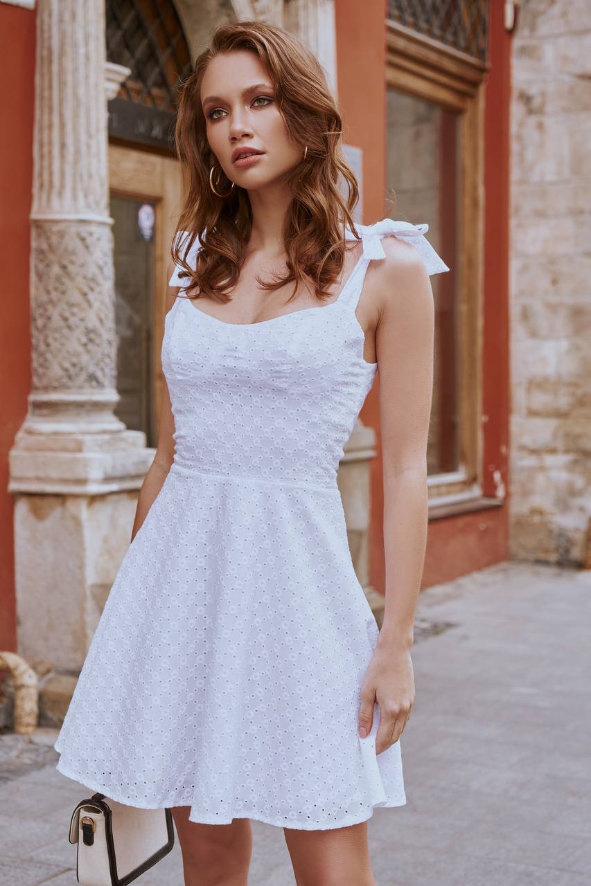 Woman wearing a white dress standing in front of a building with stone architecture.