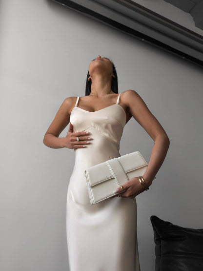 Woman in a white dress holding a clutch against a plain background