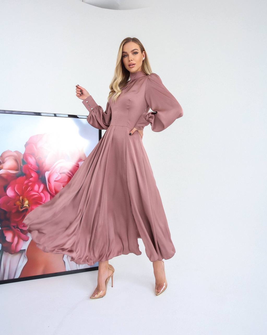 Woman wearing a long, flowing dress in a studio setting with a floral backdrop.