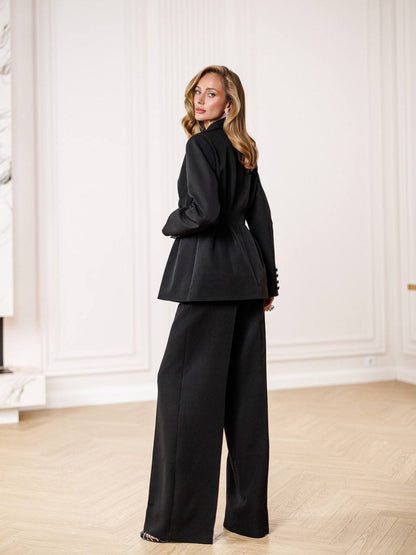 Woman wearing a black suit in an elegant room with white walls and wooden floor.