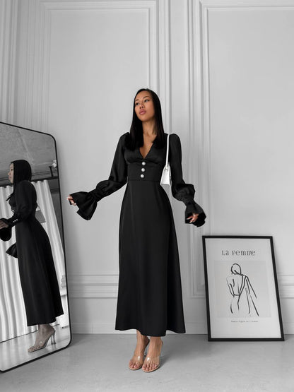 Woman wearing a black dress standing in front of a mirror in a minimalistic room.