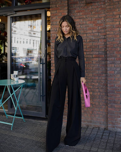 Woman in black outfit holding a pink clutch against a brick wall.