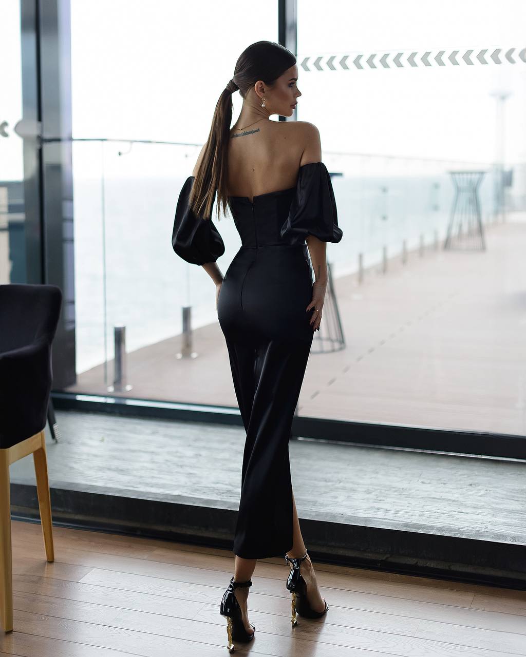 Woman in a black off-shoulder dress standing in a modern indoor setting.