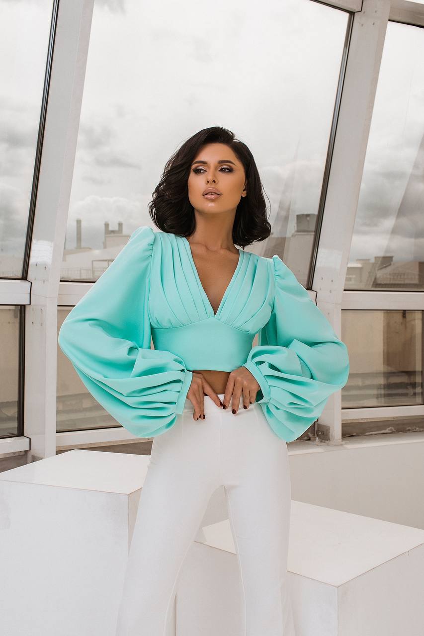 Woman wearing a light blue top with puffed sleeves and white pants in an indoor setting.