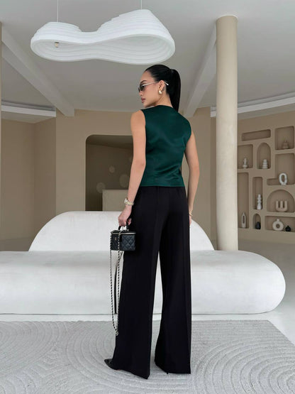 Woman in a green top and black pants standing in a modern interior setting.