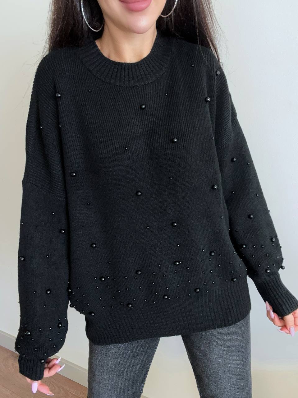 Black sweater with bead embellishments worn by a person against a neutral background