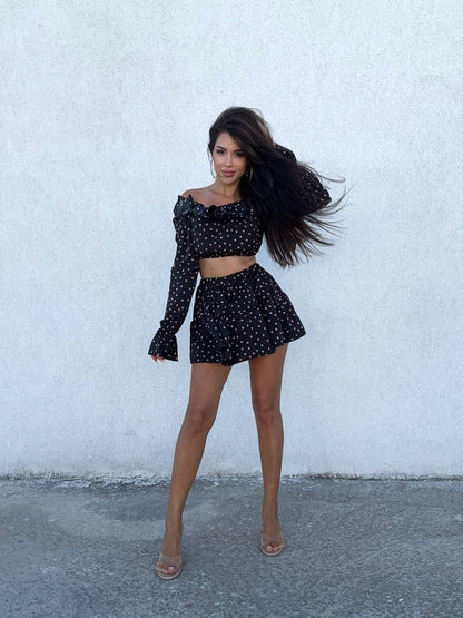 Woman wearing a black polka dot outfit against a white wall