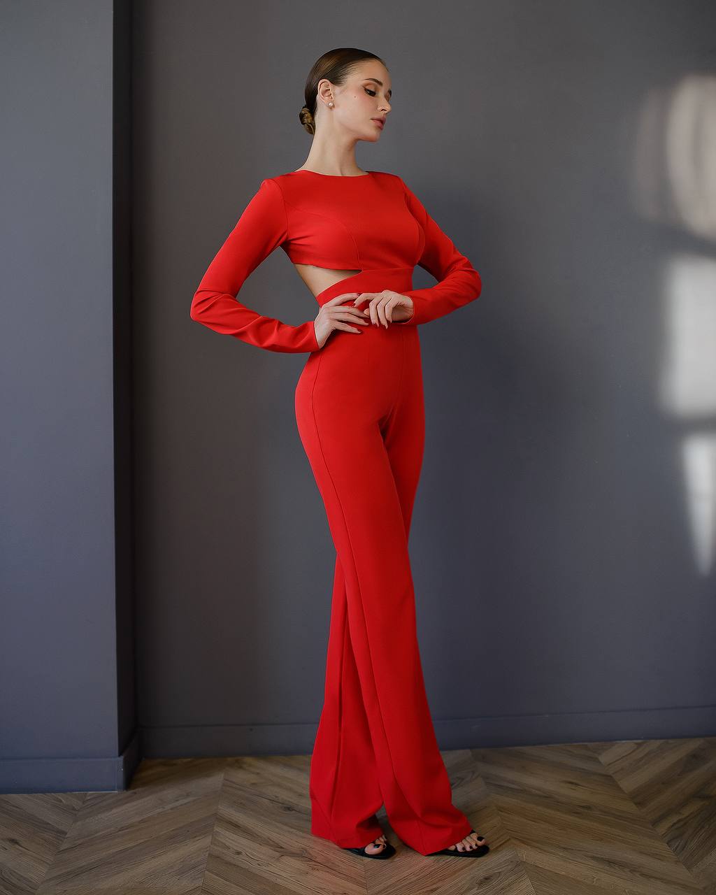 Woman wearing a red outfit standing against a gray wall.