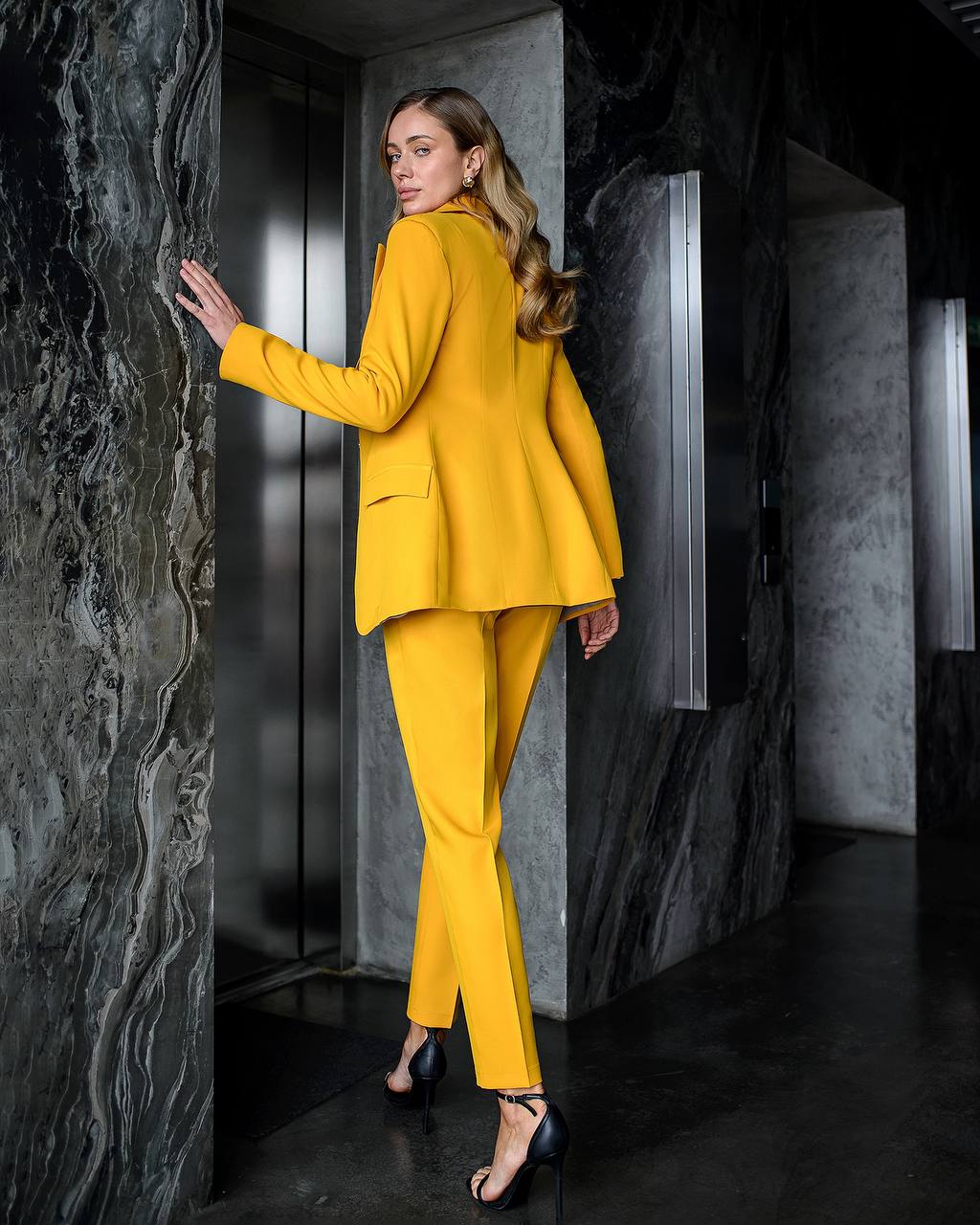 Woman in a yellow suit standing in a dark, textured room.
