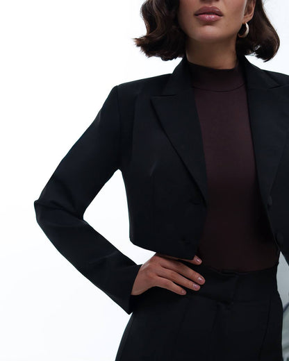 Person wearing a black blazer over a dark top on a white background
