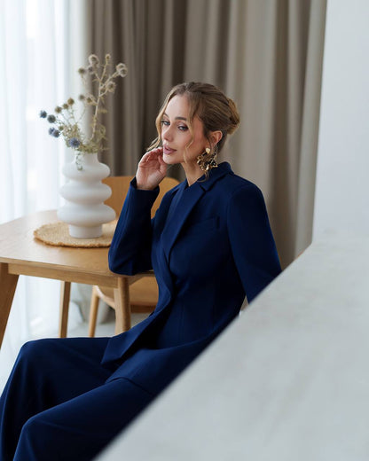 Woman in a navy blue coat sitting indoors with a neutral background
