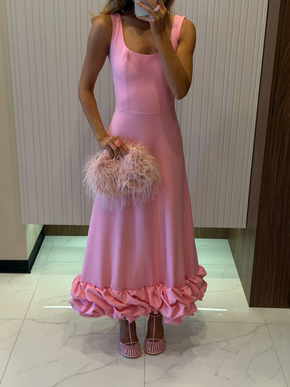 Person wearing a pink dress with ruffled hem, holding a matching pink handbag.