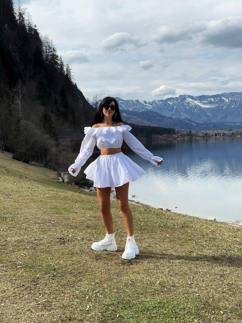 Woman in a white outfit standing by a lake with mountains in the background