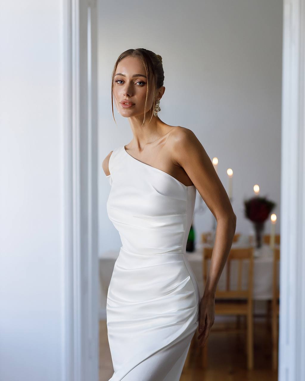 Woman wearing a white one-shoulder dress in an indoor setting.
