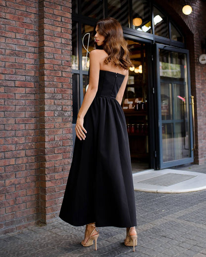Woman in a black strapless dress standing against a brick wall.