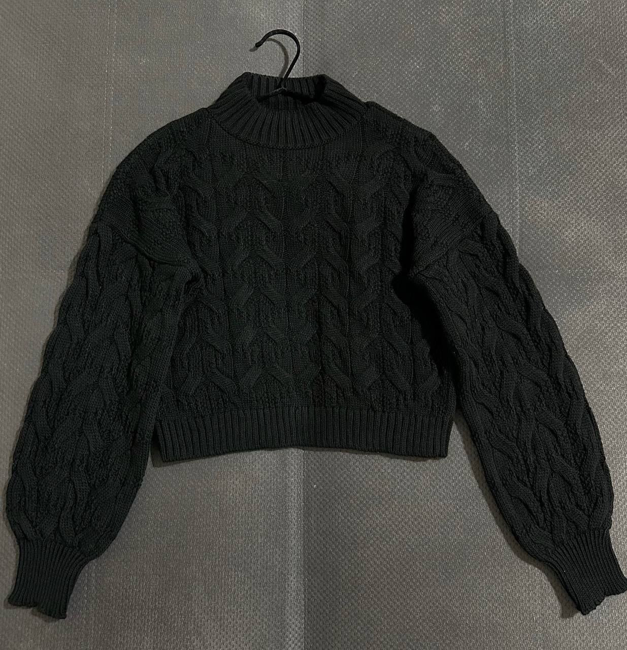 Black cable knit sweater on a hanger against a gray background