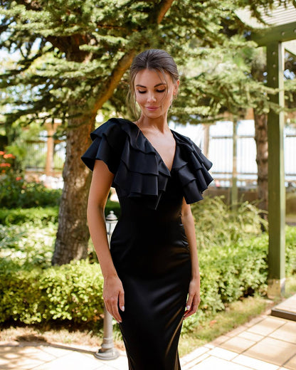 Woman wearing a black ruffled dress in an outdoor setting with greenery.