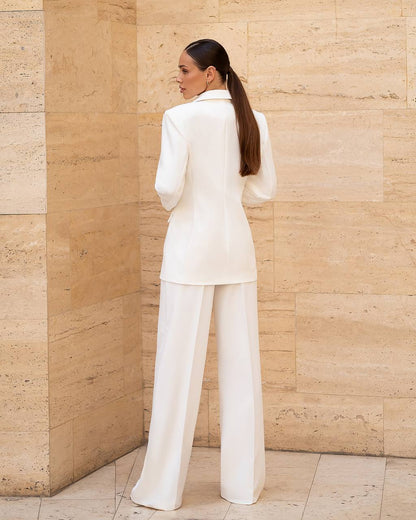 Woman in a white suit standing against a beige stone wall