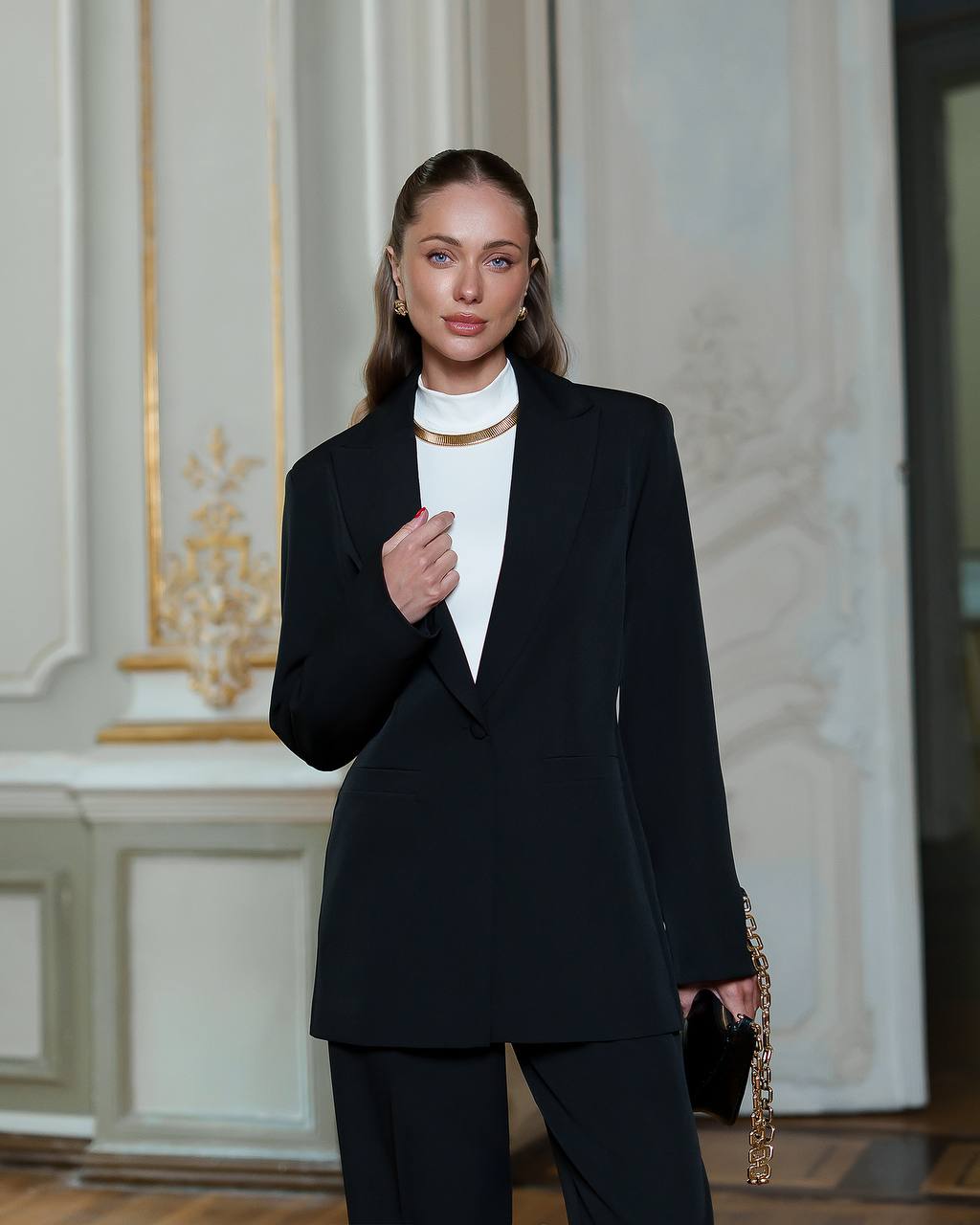 Woman in a black suit standing in an elegant interior setting