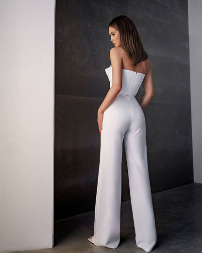 Woman wearing a white strapless jumpsuit against a dark wall.
