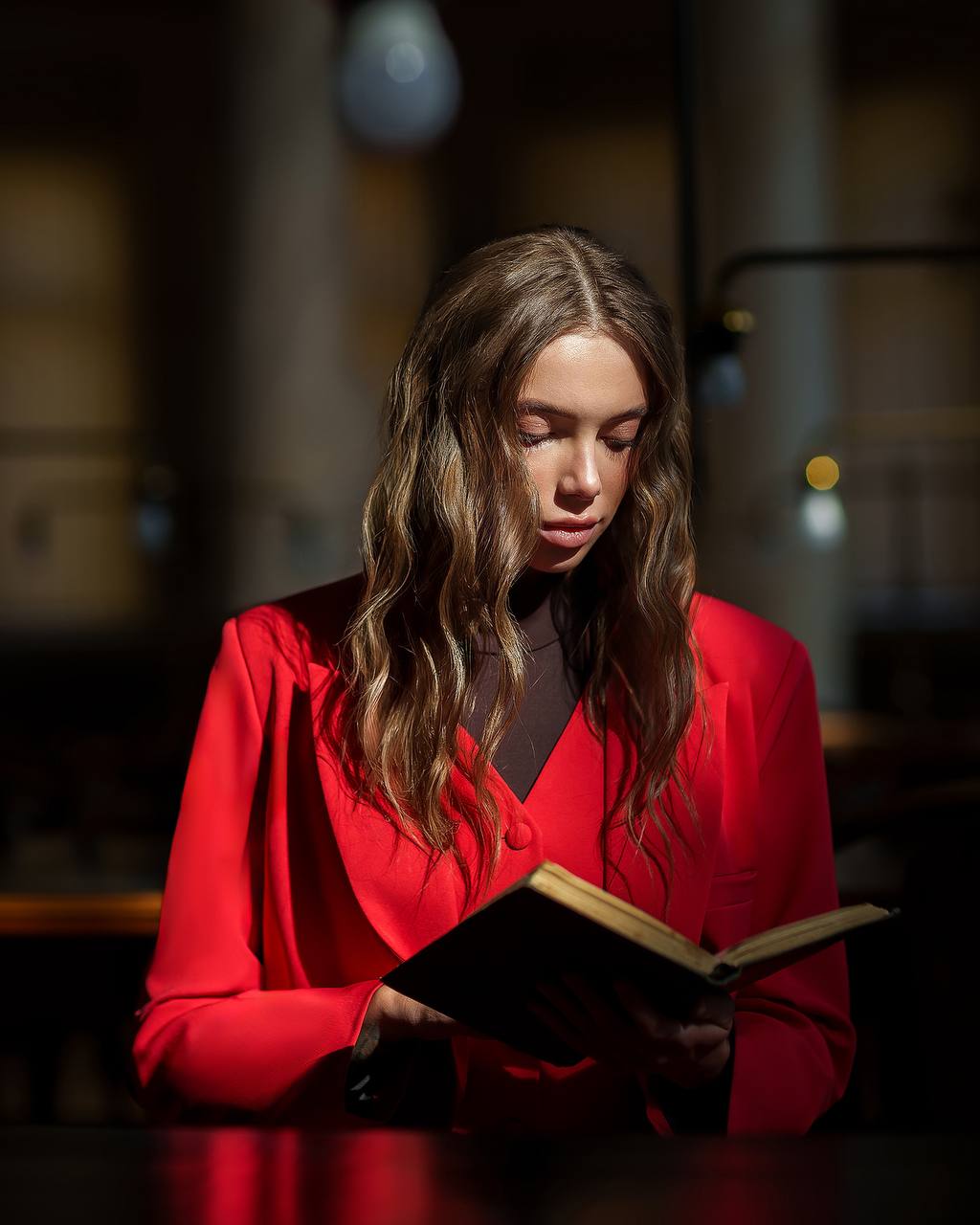 Woman in a red coat reading a book in a dimly lit room