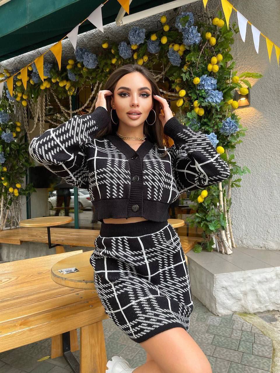 Woman in a black and white patterned outfit posing outdoors with decorative elements.