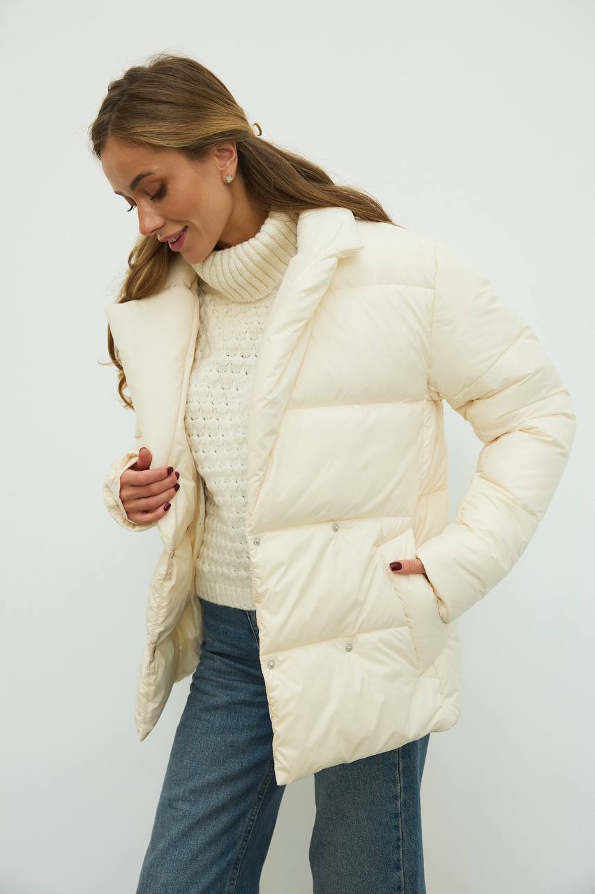Woman wearing a cream puffer jacket over a knitted sweater on a white background