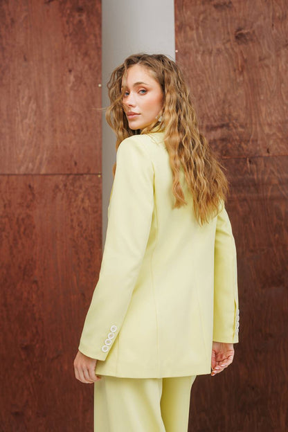 Woman wearing a light green suit against a brown wall