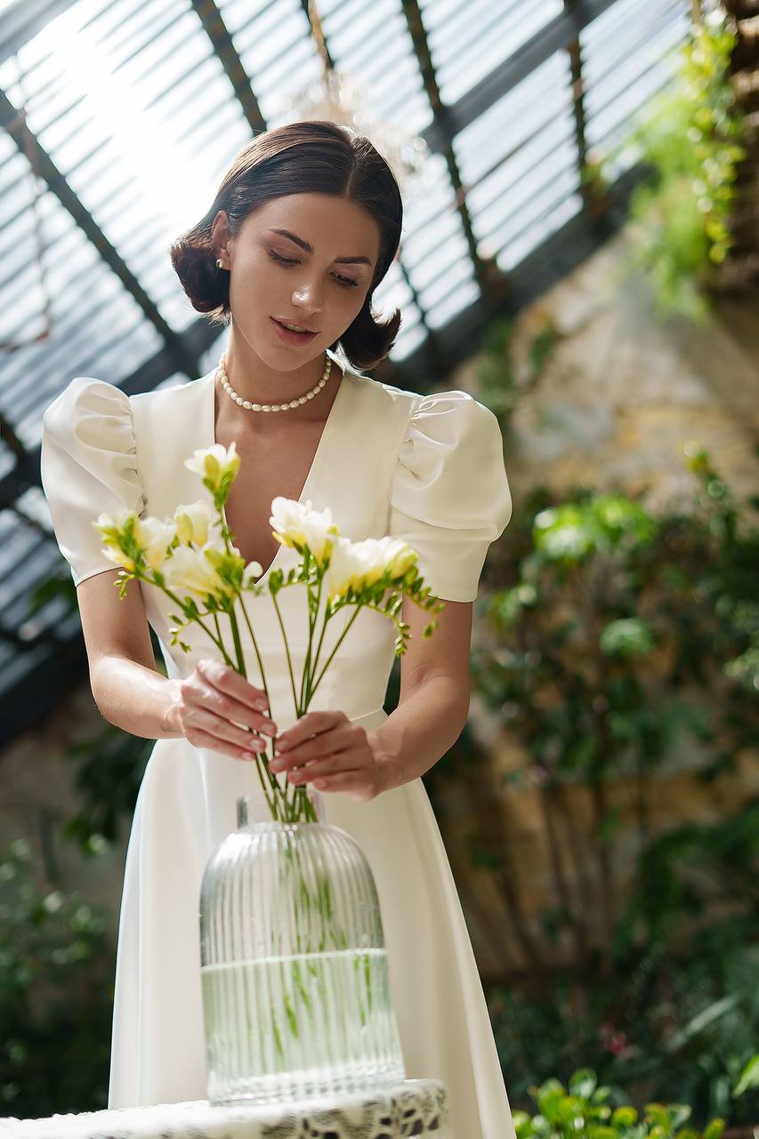 Woman in a white dress holding a vase of flowers in an outdoor setting