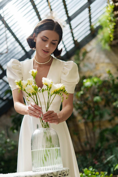 Woman in a white dress holding a vase of flowers in an outdoor setting