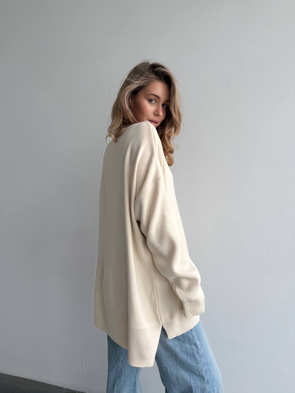 Woman wearing a beige sweater and blue jeans against a plain background