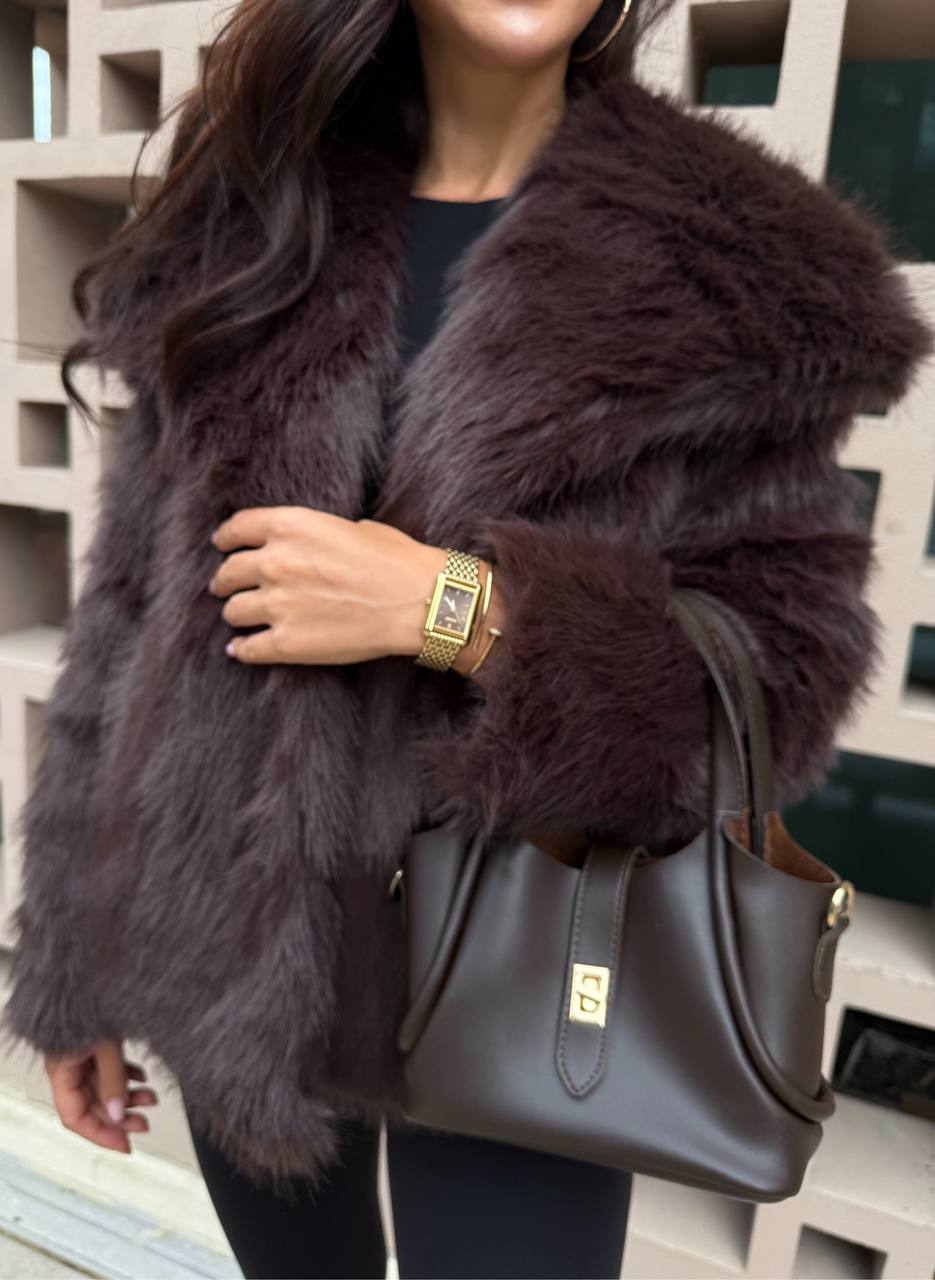 Person wearing a fur coat holding a handbag indoors