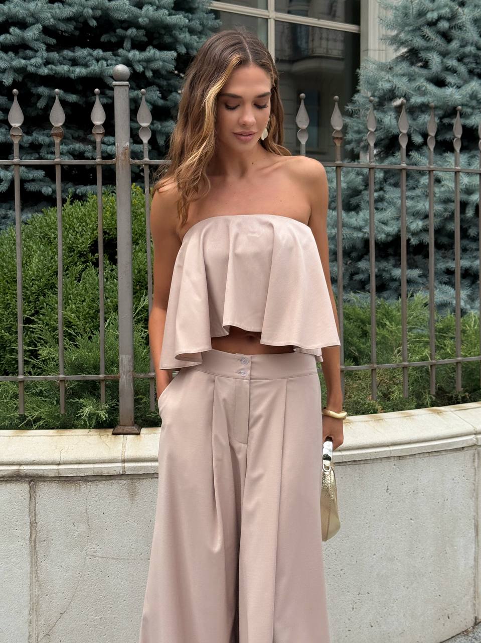 Woman wearing a light pink strapless top and wide-leg pants standing outdoors.