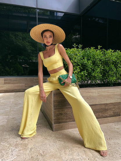 Woman in a yellow outfit with a wide-brimmed hat sitting on a bench outdoors.
