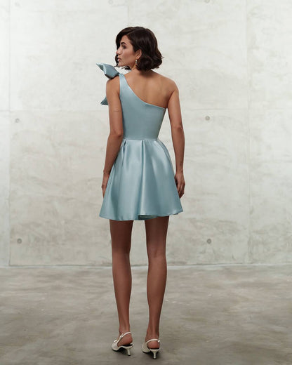 Woman wearing a light blue one-shoulder dress against a plain background