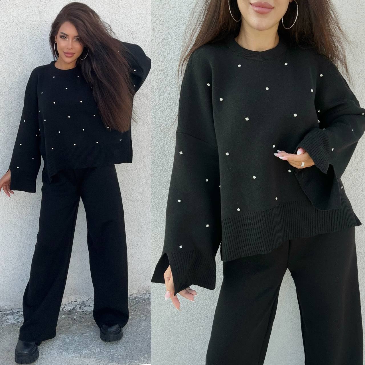 Woman wearing a black outfit with white embellishments against a gray wall.