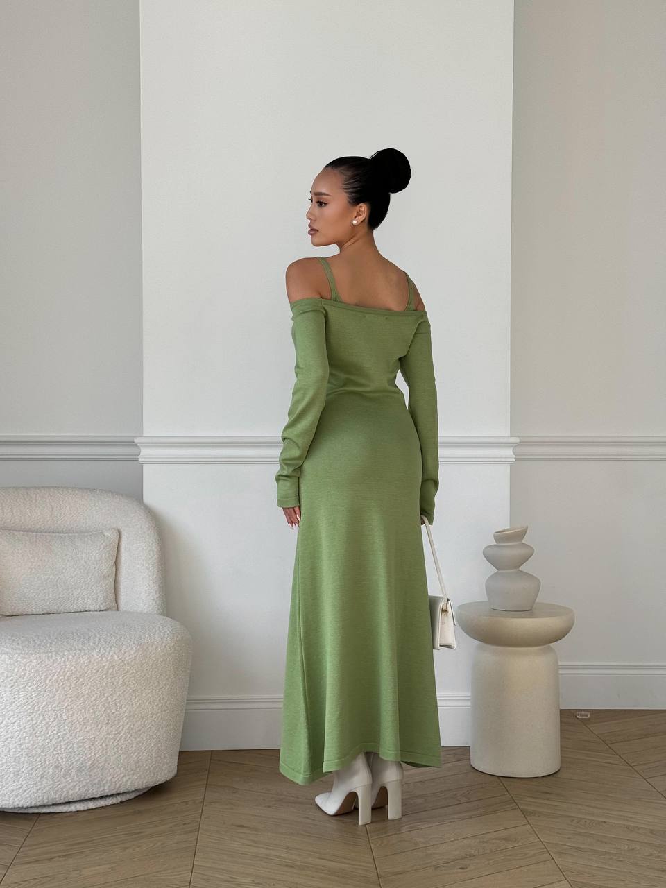 Woman in a green off-shoulder dress standing in a room with a white wall and modern decor.