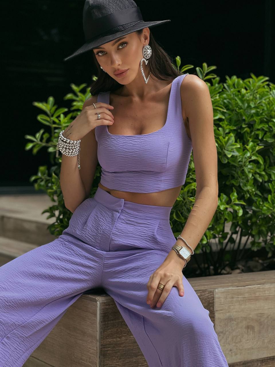 Woman in a purple outfit sitting outdoors with greenery in the background